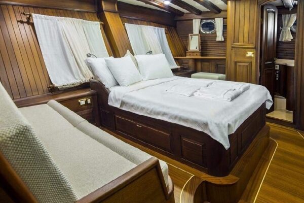 wicked-felina-gulet-photo22 Luxurious wooden cabin interior on a Gulet yacht, featuring a comfortable double bed with white linen, cozy seating, and elegant decor for premium Gulet Charter Turkey experiences.
